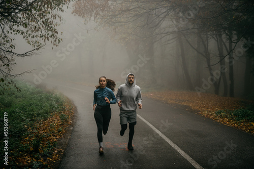 Fitness couple winter morning exercise at foggy mountain road.