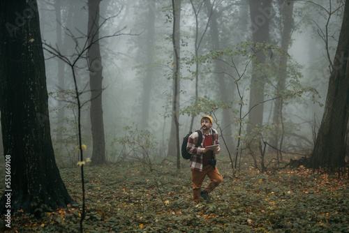 Attractive male tourist and hiker spending a weekend in the foggy forest, holding a map, wearing a backpack, and looking for directions.  © La Famiglia