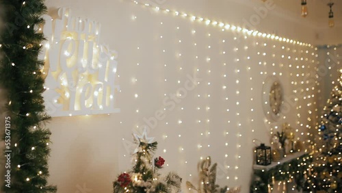 Wall decorated for Merry Christmas and Happy New Year celebration. Shiny sparkling garland lights bokeh on unfocused background with fir tree and branches