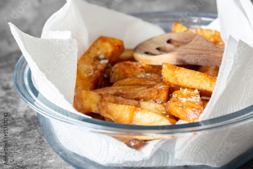 Homemade chips in a glass dish with a paper towel and wooden spoon. On a dark stone background
