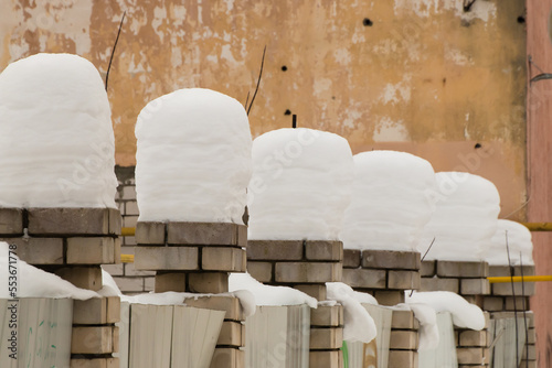 Beautiful, even, high columns of snow on brick pillars. An even row of small snowdrifts against the background of a shabby wall. Urban winter landscape. Cloudy winter day, soft light.