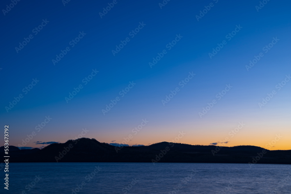 夜明けの空は美しいグラデーションに山のシルエットが際立つ湖の風景。