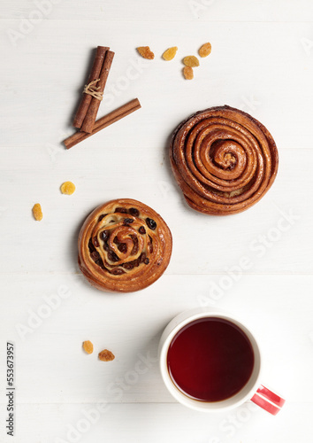 Sweet buns with raisins and cinnamon, a cup with a hot drink and autumn leaves. On a light wooden background,flatlay photo