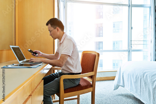 Man using laptop and phone in bedroom