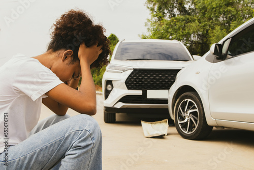 African american woman sitting with head down stressed driving recklessly hitting the front of the car and damaging the bumper. Sitting with her head watching the damage her car was out of warranty. photo