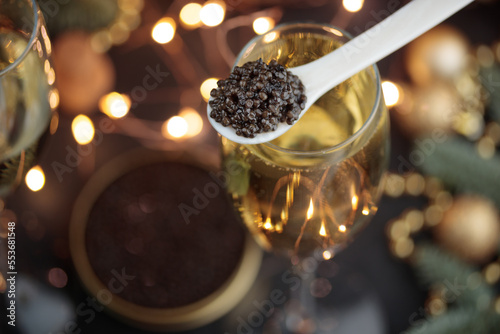 Black caviar in a mother-of-pearl spoon and glass of champagne with Christmas decoration