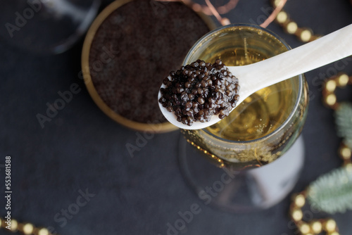 Black caviar in a mother-of-pearl spoon and glass of champagne with Christmas holiday decoration, gold bokeh for New Year Eve party celebration, expensive delicious appetizer sea food