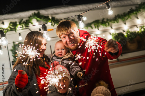 Happy large family celebrates christmas in nature and holds sparklers. Parents with three sons travels in a mobile home.
