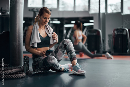 Pretty woman working out in a gym  making pause and using smartphone. Adult pretty sporty lady with beautiful shaped body.