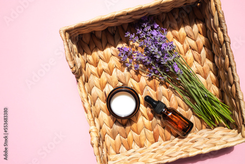 Organic moisturizer with natural lavender and a glass jar of lavender oil in a wicker basket on a pink background. flat lay, place for text.