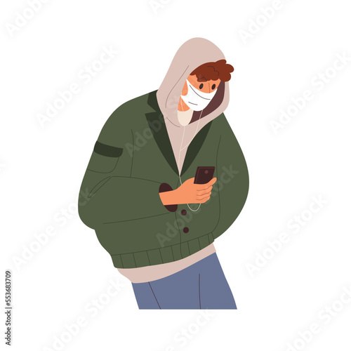 Man in face mask, listening to music with earphones, holding mobile smart pho...