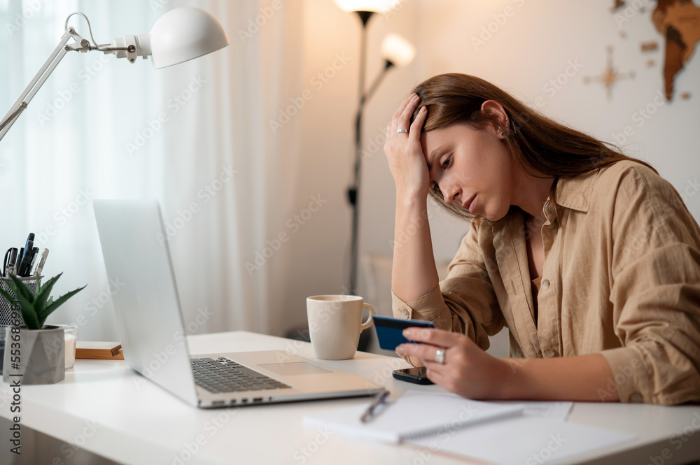Sleepy lady sitting at desk with laptop, holding credit card Sleepy lady sitting at desk with laptop, holding credit card