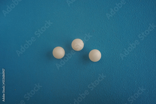 Three ping pong tennis balls lie in a row on a blue background with a close-up view from above. Game for leisure. Sport equipment. International competition. Table tennis. Healthy lifestyle