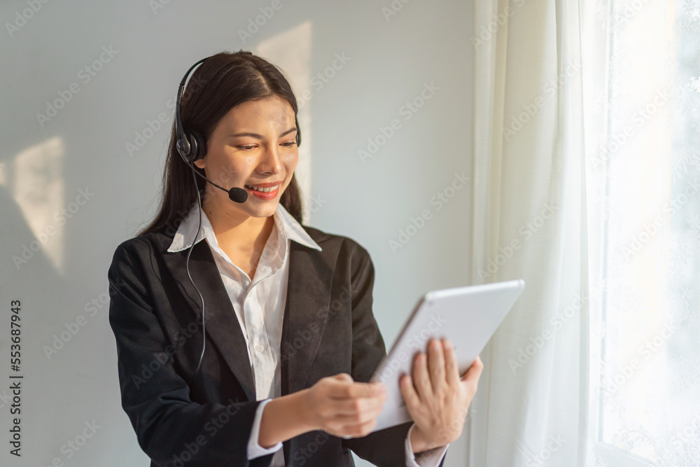 Young beautiful smart asian lady businesswoman working on digital tablet and providing customer support assistance over her wired microphone headset in an office Young beautiful smart asian lady businesswoman working on digital tablet and providing customer support assistance over her wired microphone headset in an office