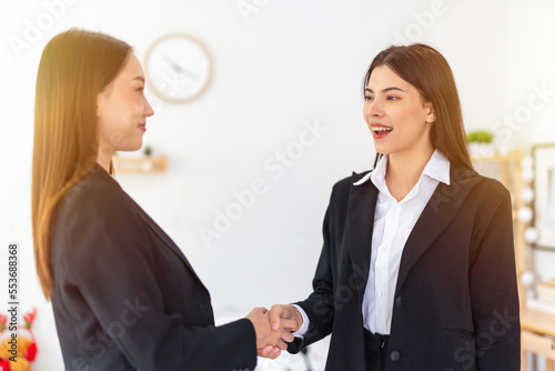 Two young smart beautiful asian lady businesswomen smiling and have a hand shake to commemorate a deal successful in a meeting room