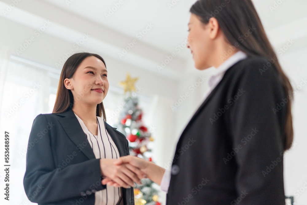 Two young smart beautiful asian lady businesswomen smiling and have a hand shake to commemorate a deal successful in a meeting room in front a Christmas tree Two young smart beautiful asian lady businesswomen smiling and have a hand shake to commemorate a deal successful in a meeting room in front a Christmas tree