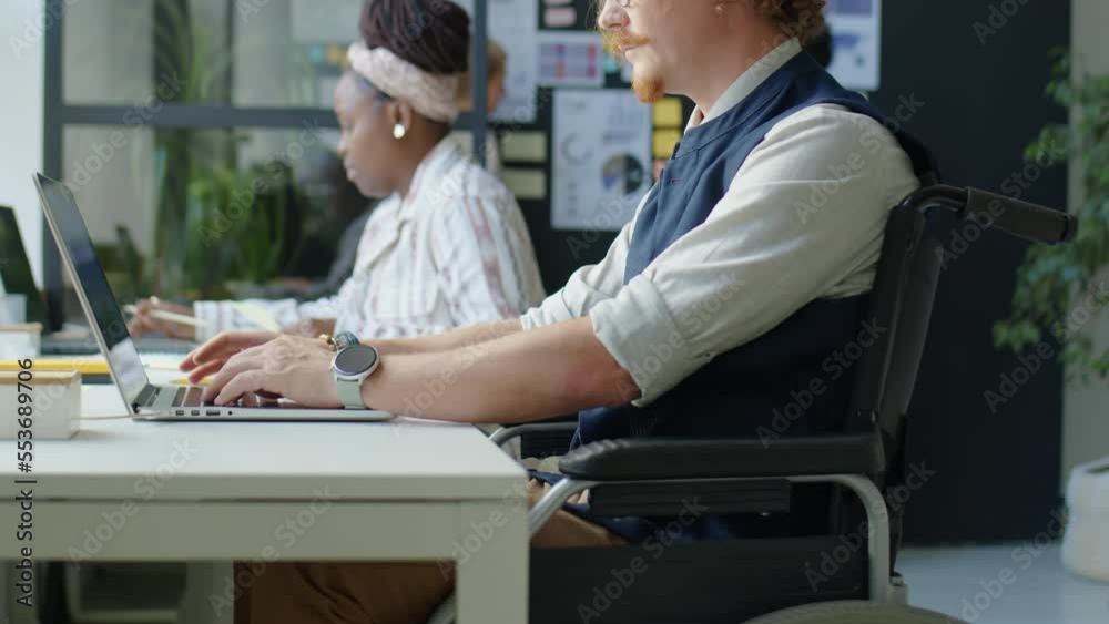 Cropped shot of businessman in wheelchair typing on laptop at desk while working in office Cropped shot of businessman in wheelchair typing on laptop at desk while working in office