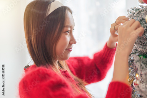 Young beautiful friendly asian female lady with red long sleeve sweater shirt and cute headband posing different look cheerfully with a nicely decorated Christmas tree in a room