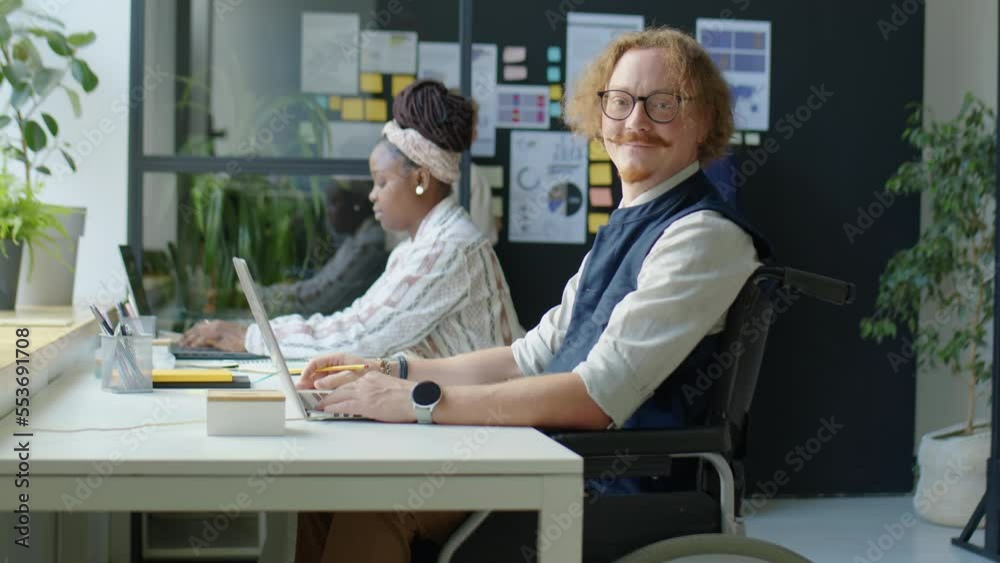 Portrait of Caucasian businessman in wheelchair posing for camera with smile at workplace in open space office Portrait of Caucasian businessman in wheelchair posing for camera with smile at workplace in open space office