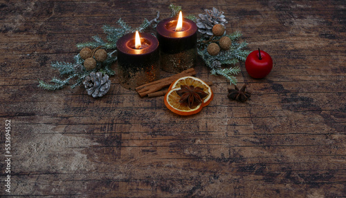 Nostalgische Advent und Weihnachtsdekoration: Zwei brennende Kerzen mit Tannenzweigen,Apfel und Zimtstangen auf einem alten schäbigen Hozhintergrund.