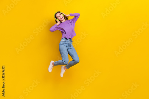 Full length photo of excited carefree person jumping hands touch wireless headphones isolated on yellow color background