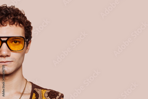 Billede på lærred Half face portrait of young fashion man with curly hair, wears orange sunglasses at studio isolated over beige background