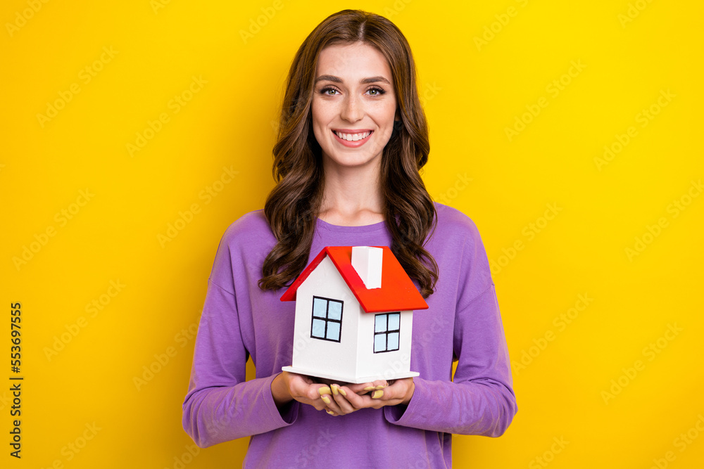 Photo of shiny adorable lady wear violet sweater holding arms small red roof house isolated yellow color background Photo of shiny adorable lady wear violet sweater holding arms small red roof house isolated yellow color background