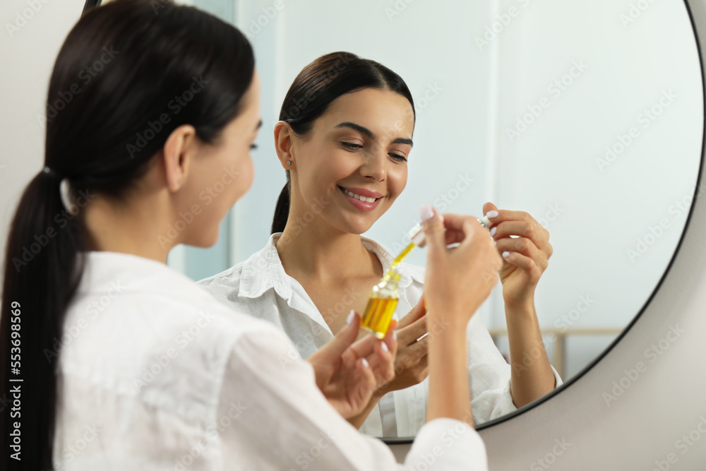 Young woman with bottle of essential oil near mirror Young woman with bottle of essential oil near mirror