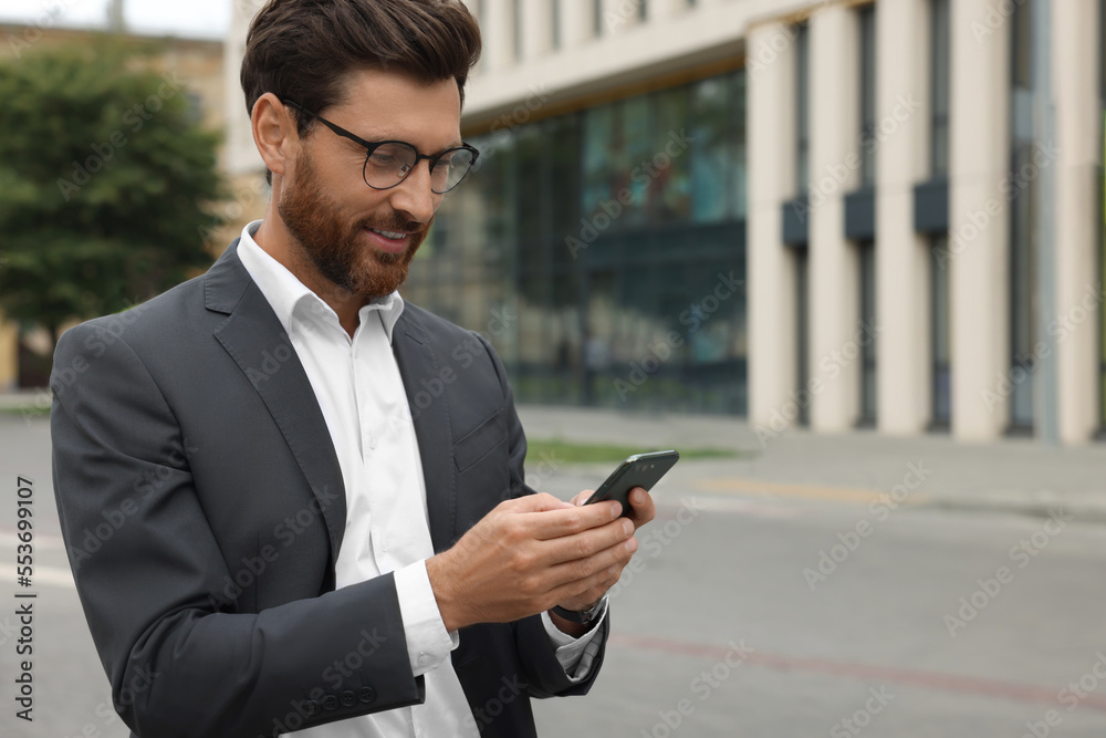 Handsome businessman with smartphone on city street, space for text Handsome businessman with smartphone on city street, space for text