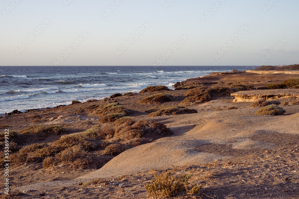 Sunrise on the beach on a summer day. Shore, rocky beach. Textures of the stones on the shore. Ocean waves in the background. Calm clear sky, orange color. El medano, Tenerife, Canary Islands, Spain. Sunrise on the beach on a summer day. Shore, rocky beach. Textures of the stones on the shore. Ocean waves in the background. Calm clear sky, orange color. El medano, Tenerife, Canary Islands, Spain.