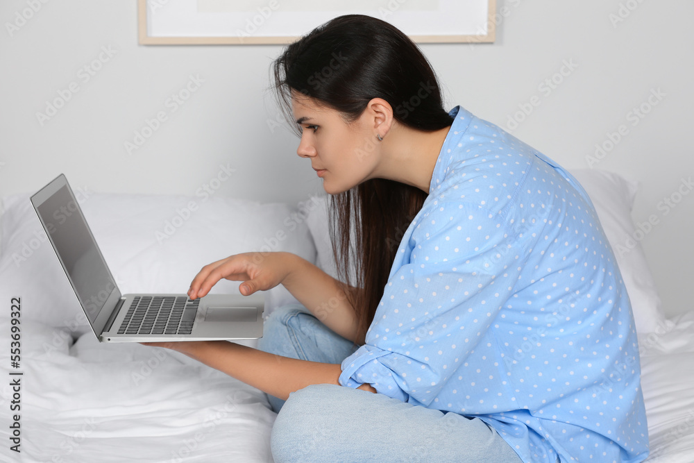 Young woman with bad posture using laptop while sitting on bed at home. Symptom of scoliosis Young woman with bad posture using laptop while sitting on bed at home. Symptom of scoliosis