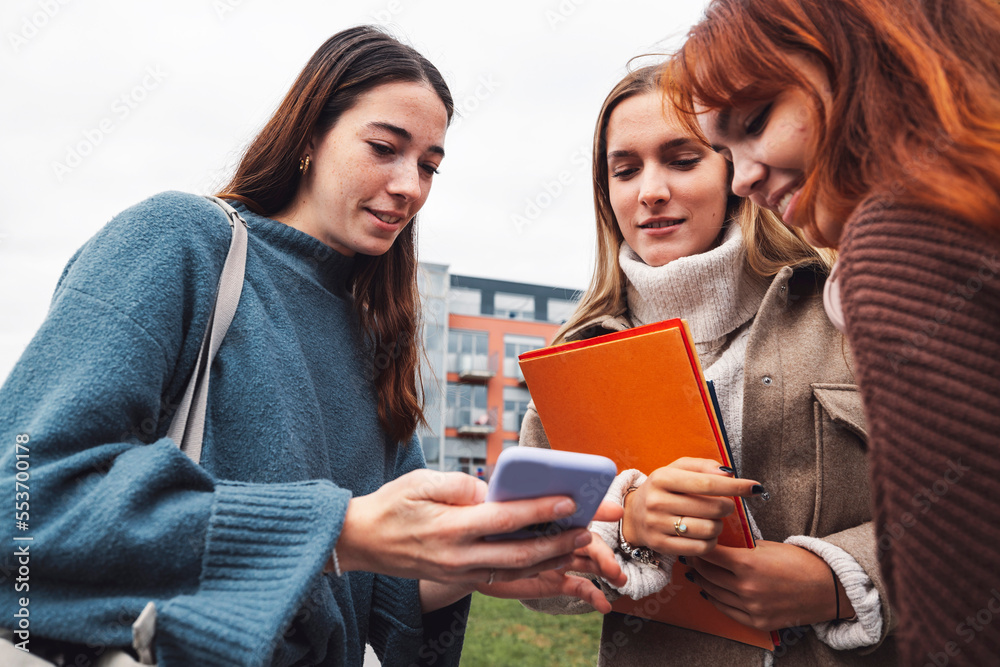 Low angle view of three college friends looking at a phone, discussing something Low angle view of three college friends looking at a phone, discussing something