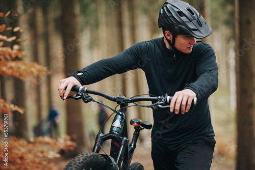 Young man pushing his mountain bike up a forest trail photo