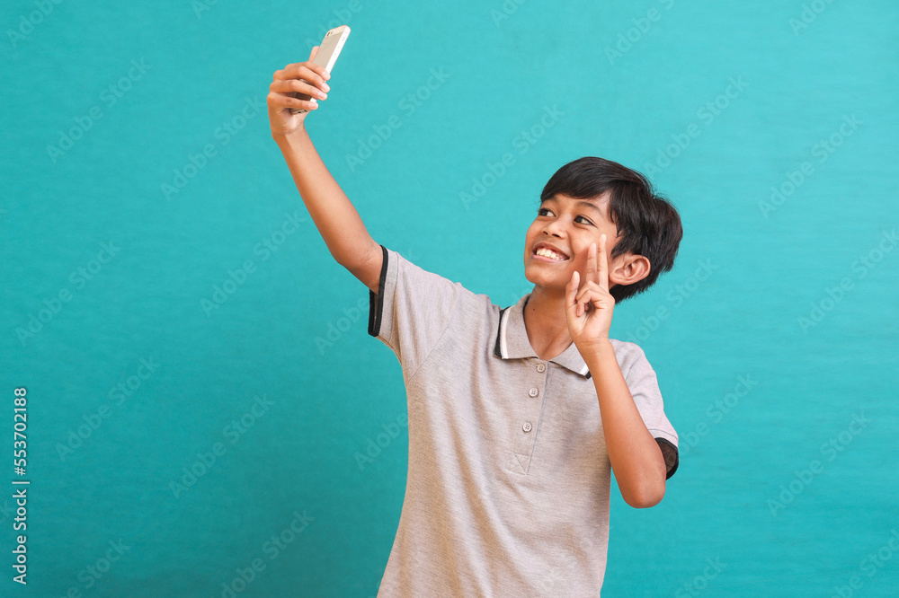 Cute Asian kid wearing casual clothes, taking a selfie to send it to friends and followers or post it on his social media.