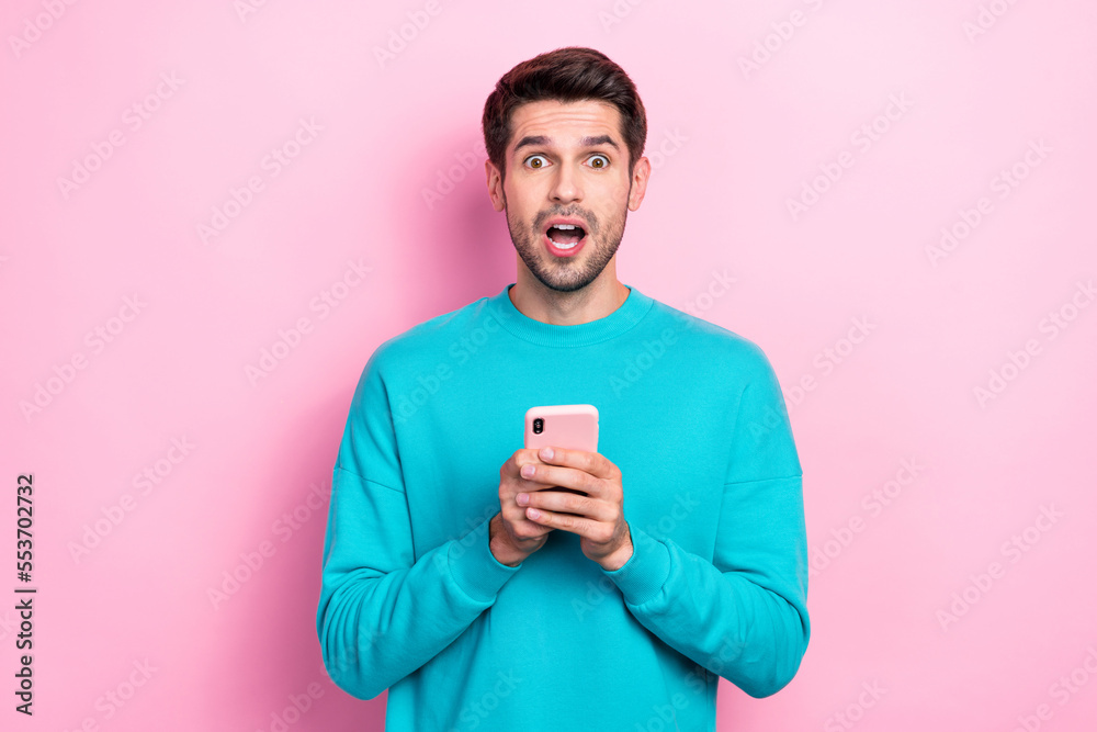 Portrait of young excited funny guy wear blue sweatshirt hold phone open mouth hold smartphone shock news isolated on pink color background Portrait of young excited funny guy wear blue sweatshirt hold phone open mouth hold smartphone shock news isolated on pink color background