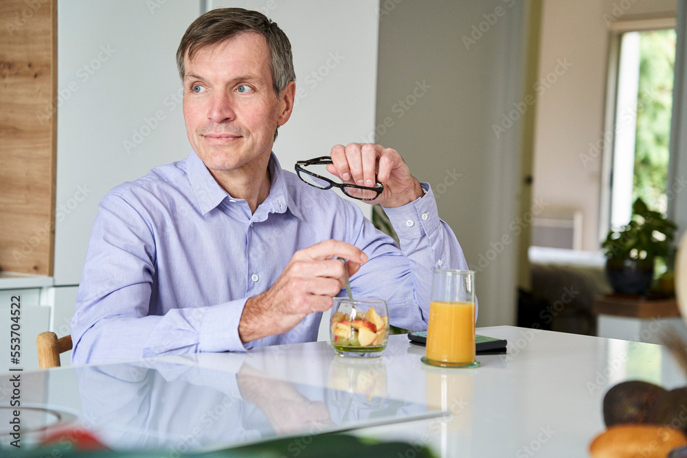 Middle-aged professional man having breakfast on kitchen counter at home Middle-aged professional man having breakfast on kitchen counter at home