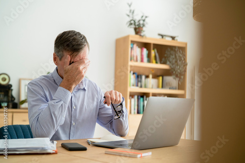 Stressed senior businessman with hand on face doing home office © PhotoAlto