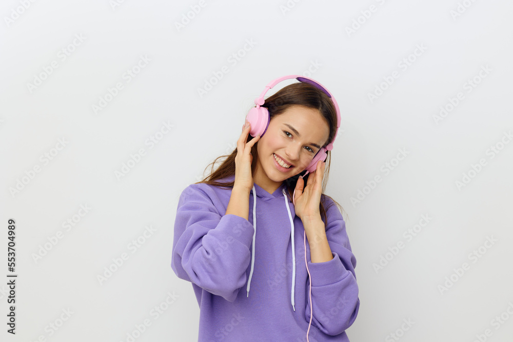 horizontal studio photo of a happy, joyful woman in a purple tracksuit listening to music holding her pink headphones with both hands and smiling broadly looking at the camera horizontal studio photo of a happy, joyful woman in a purple tracksuit listening to music holding her pink headphones with both hands and smiling broadly looking at the camera