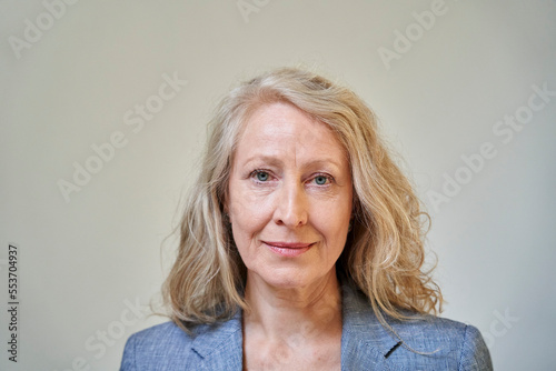 Senior blonde woman looking at the camera while standing against white background © PhotoAlto