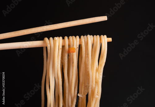 Noodles hang on a chopstick on a black background. A dish of Asian cuisine with soy sauce.