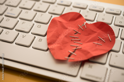 Foto Seriously injured red heart paper with surgical skin stapler on white keyboard computer background