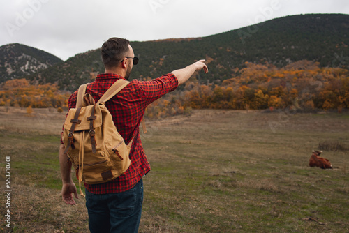 Side view of hiker tourist pointing hand on right direction. Young man with backpack looking for directions in mountain.