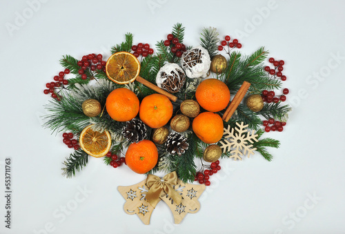 Festive Christmas border from conifer tree branches ,wooden bells , fresh viburnum berries, tangerines, gold nuts ,cones, rattan handmade snowballs on white background. Top view .Free copy space