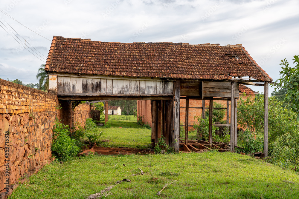 Ruins of an old wooden building and clay tiles on a grassy floor, with a red stone wall in an old coffee farm. Ruins of an old wooden building and clay tiles on a grassy floor, with a red stone wall in an old coffee farm.