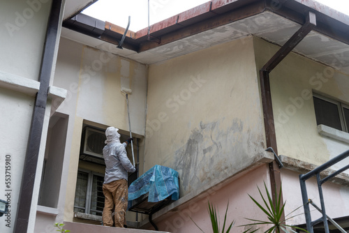 Painter worker adding undercoat foundation paint onto wall with roller at residential building in renovation