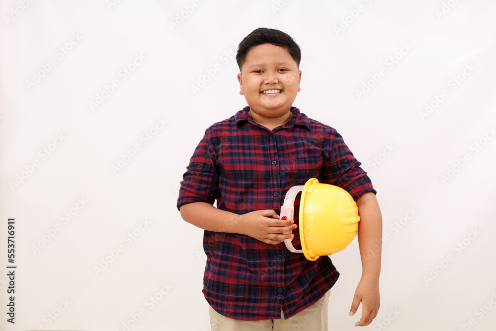 Happy asian boy standing while carrying engineer helmet. Kid's aspirations concept. Isolated on white background
