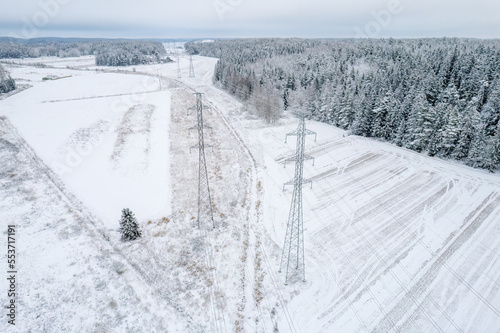 The power line passes through snow-covered trees and snowy fields on a cold frosty day in Finland. Aerial view. © Finmiki