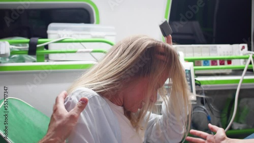 Side view of woman shouting and pushing during labor contractions lying on stretcher in modern ambulance with paramedics. Young caucasian female pregnant patient suffering from pain during delivery.