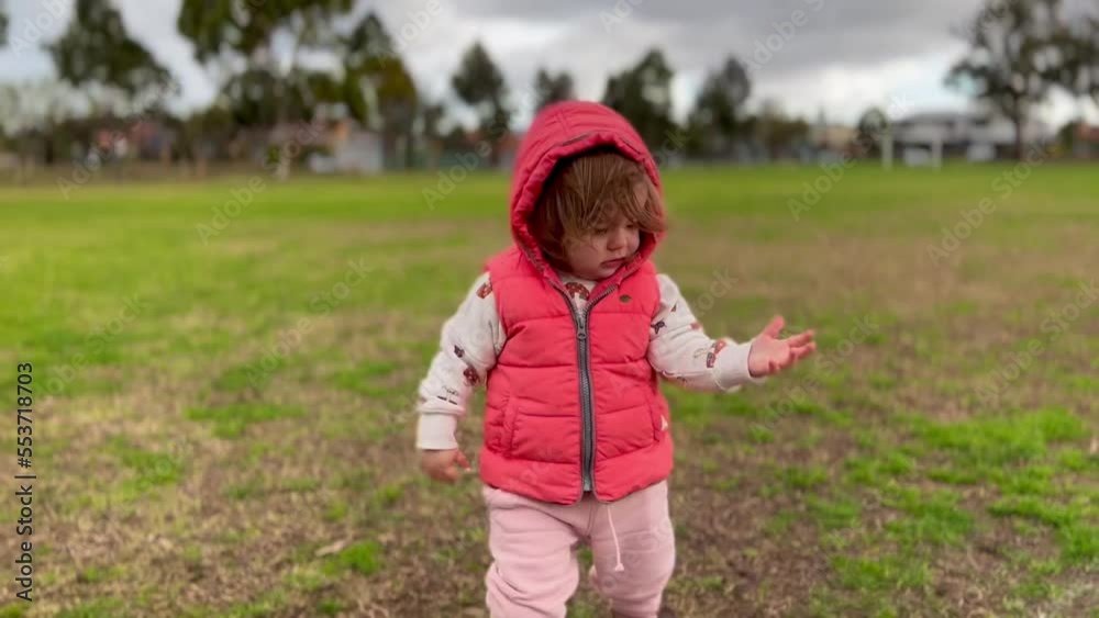 Curious caucasian toddler walking in a park with a bright pink vest on Curious caucasian toddler walking in a park with a bright pink vest on