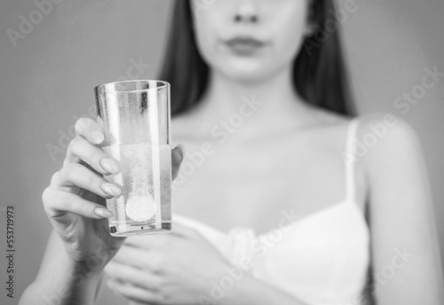 Woman taking drugs to releave headache. Brunette take some pills, holds glass of water, isolated on blue. Black and white photo